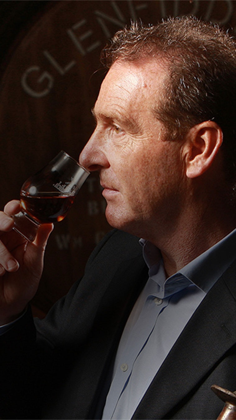 Man smelling the aroma of whisky with whisky barrels in background