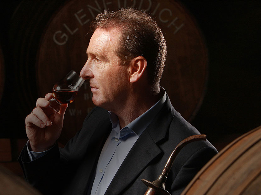 Man smelling the aroma of whisky with whisky barrels in background