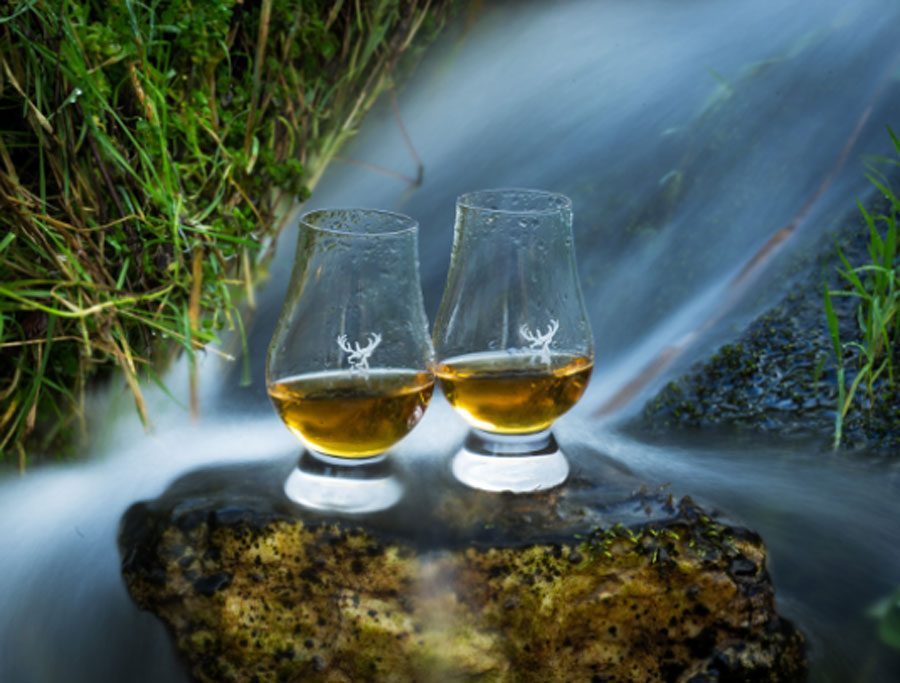 2 drams of whisky on a rock behind a water stream