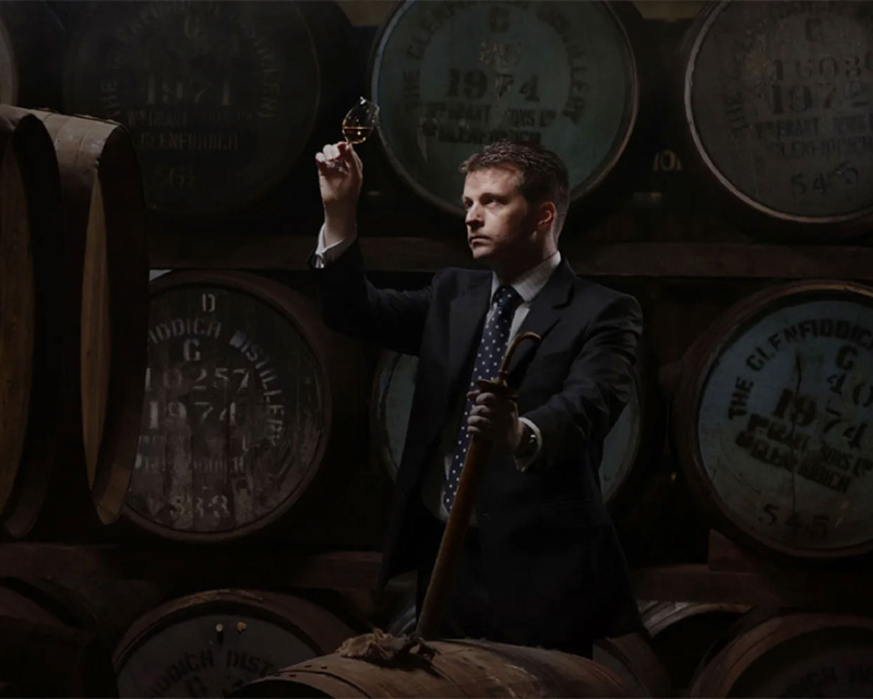 Man inspecting a dram of whisky in a distillery warehouse